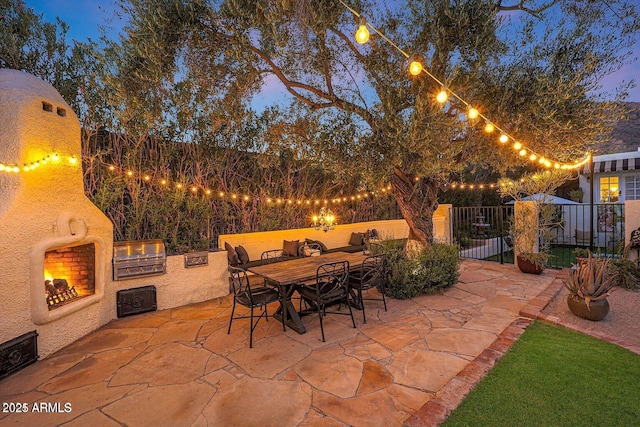 patio terrace at dusk with exterior kitchen and a fireplace