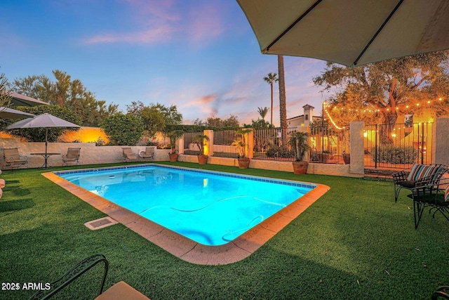 pool at dusk featuring a lawn