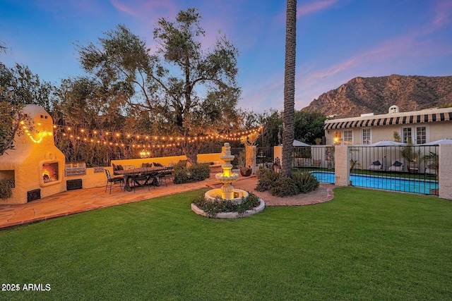 yard at dusk with a mountain view, a fireplace, a fenced in pool, and a patio area