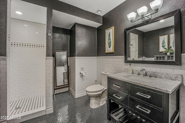 bathroom featuring tiled shower, toilet, tile walls, vanity, and tile patterned flooring