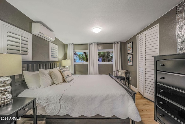 bedroom featuring a wall unit AC, light hardwood / wood-style floors, and a textured ceiling