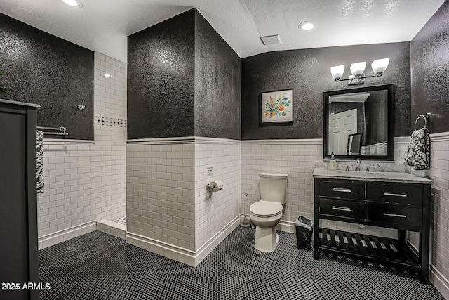 bathroom featuring a tile shower, tile walls, tile patterned flooring, vanity, and toilet