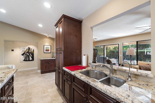 kitchen with light stone counters, sink, dark brown cabinets, and vaulted ceiling