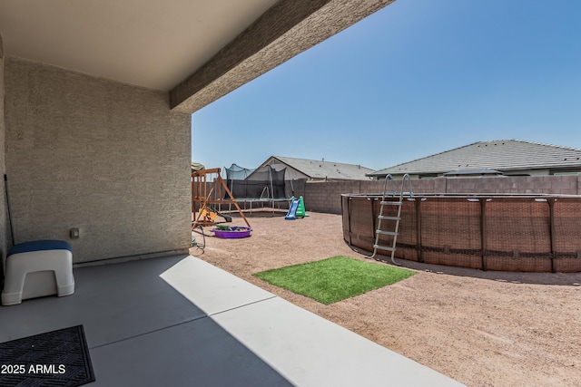 view of yard featuring a fenced backyard, a trampoline, a playground, and a patio