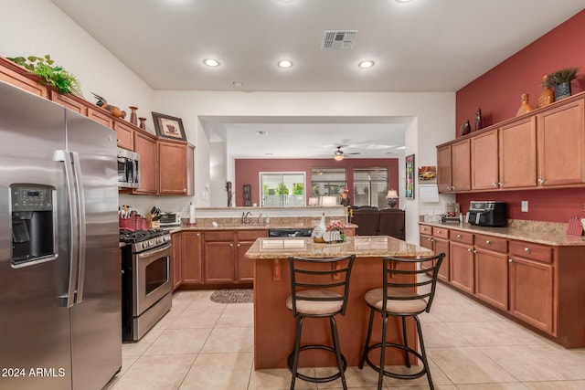 kitchen with ceiling fan, light stone countertops, appliances with stainless steel finishes, a kitchen island, and a kitchen bar