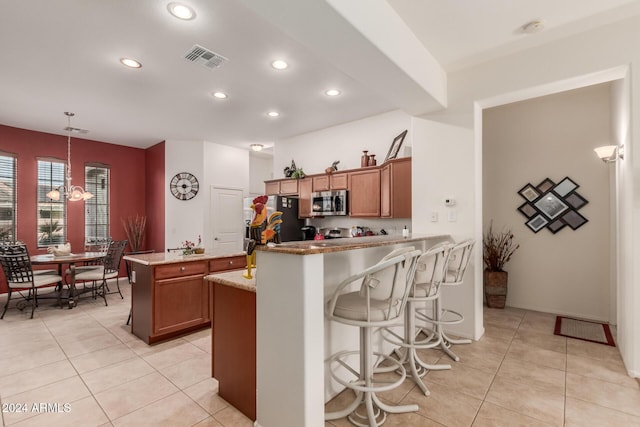 kitchen featuring light stone countertops, kitchen peninsula, decorative light fixtures, light tile patterned floors, and appliances with stainless steel finishes