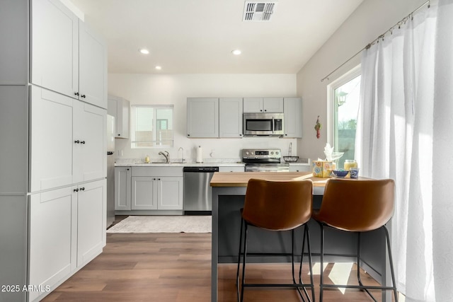 kitchen with wood-type flooring, a kitchen breakfast bar, appliances with stainless steel finishes, sink, and white cabinets