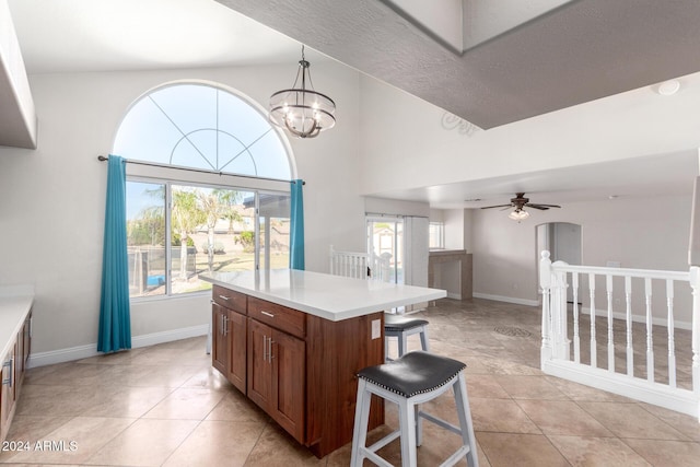 kitchen featuring a high ceiling, a kitchen island, decorative light fixtures, light tile patterned floors, and ceiling fan with notable chandelier