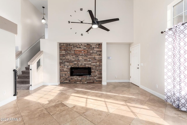 unfurnished living room with a stone fireplace, ceiling fan, a towering ceiling, and light tile patterned floors