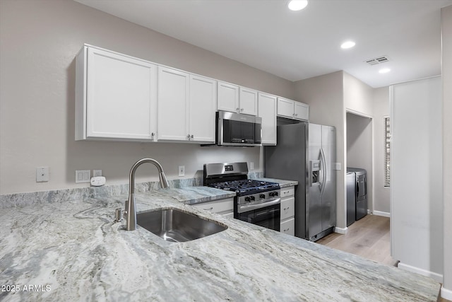 kitchen featuring light stone countertops, white cabinetry, stainless steel appliances, washing machine and clothes dryer, and sink