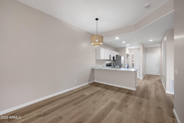 kitchen featuring decorative light fixtures, light hardwood / wood-style floors, kitchen peninsula, white cabinetry, and appliances with stainless steel finishes