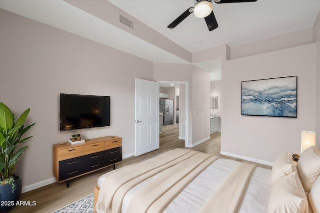 bedroom featuring stainless steel refrigerator with ice dispenser, ceiling fan, connected bathroom, and light hardwood / wood-style flooring