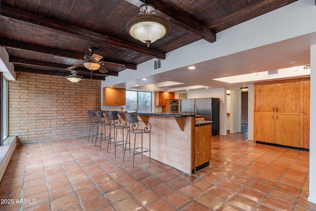 kitchen with stainless steel appliances, a breakfast bar, wood ceiling, kitchen peninsula, and brick wall