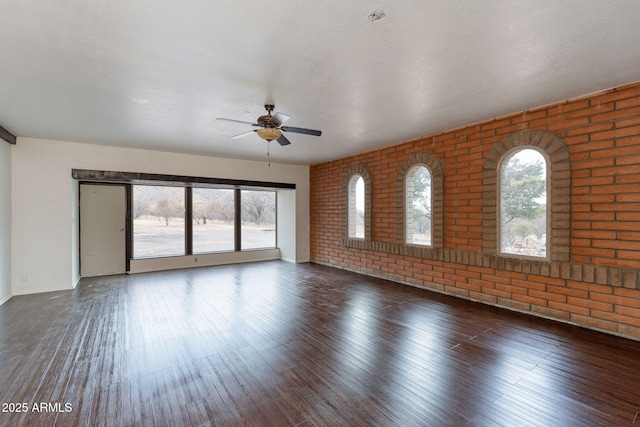 unfurnished room with brick wall, dark hardwood / wood-style floors, a textured ceiling, and ceiling fan