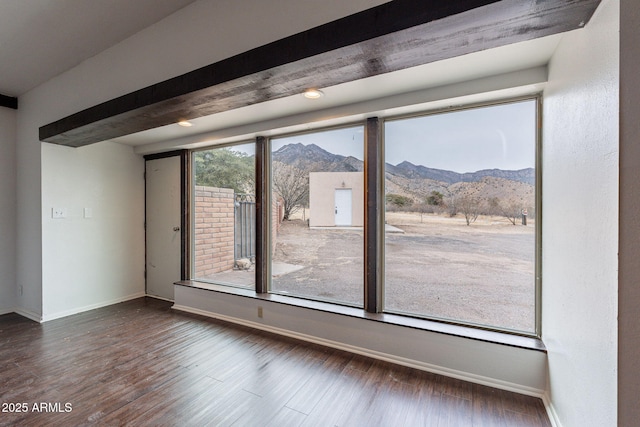 empty room with a mountain view, dark wood-type flooring, and beamed ceiling