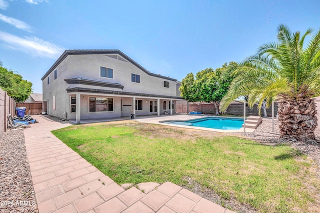 rear view of property with a fenced in pool, a patio area, and a lawn