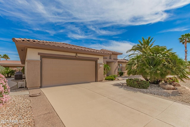 mediterranean / spanish house with an attached garage, central AC, a tile roof, stucco siding, and concrete driveway