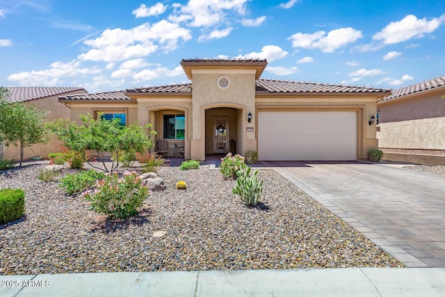 mediterranean / spanish-style house featuring stucco siding, a garage, decorative driveway, and a tiled roof