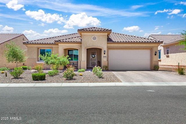 mediterranean / spanish home featuring stucco siding, a garage, a tiled roof, and concrete driveway