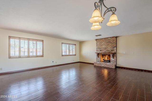 unfurnished living room with dark wood-type flooring, a notable chandelier, and a brick fireplace