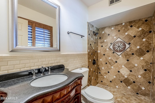 bathroom featuring vanity, toilet, a tile shower, and tile walls