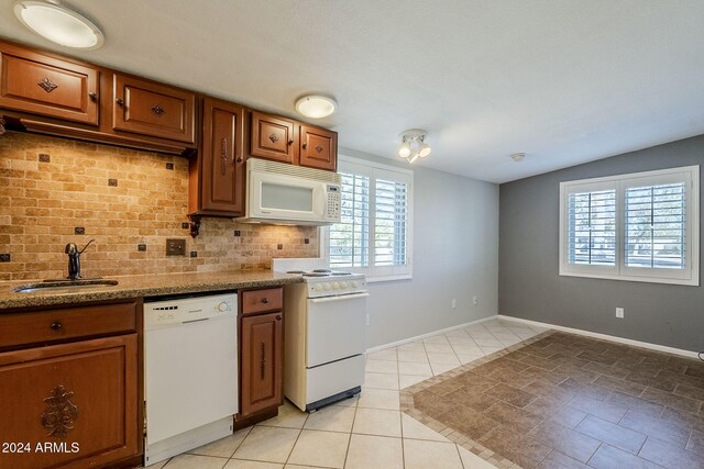 kitchen with light stone countertops, backsplash, white appliances, sink, and light tile patterned floors