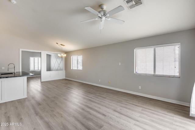 unfurnished living room featuring light wood finished floors, visible vents, baseboards, ceiling fan with notable chandelier, and a sink