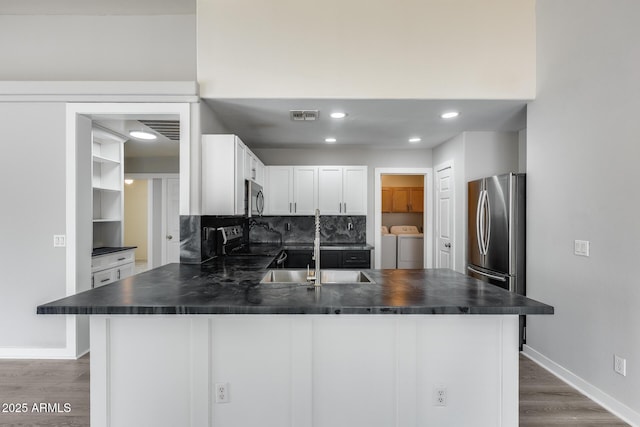 kitchen featuring visible vents, a peninsula, separate washer and dryer, appliances with stainless steel finishes, and dark countertops