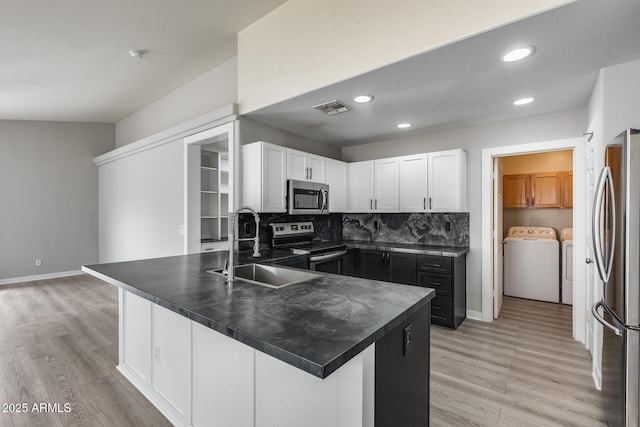 kitchen featuring visible vents, washing machine and clothes dryer, a sink, appliances with stainless steel finishes, and dark countertops