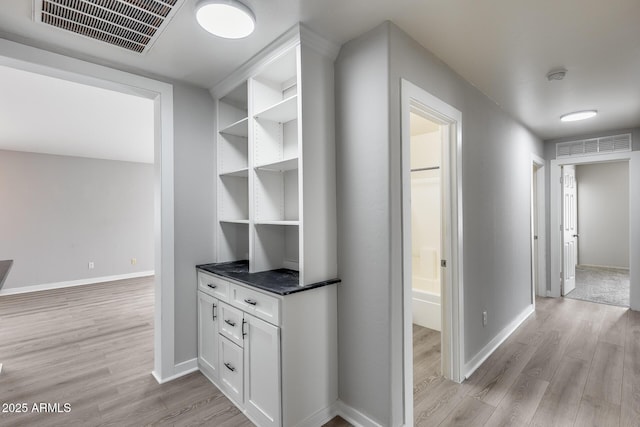 corridor with baseboards, visible vents, and light wood-type flooring