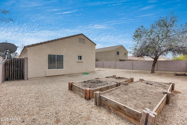 back of house with stucco siding, a tile roof, a fenced backyard, and a garden