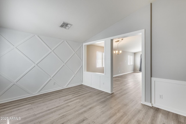 spare room with visible vents, a decorative wall, light wood-type flooring, lofted ceiling, and a notable chandelier