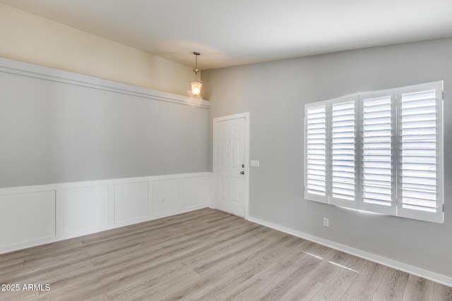 unfurnished dining area with wood finished floors, wainscoting, and a decorative wall