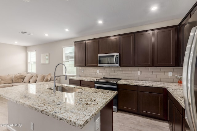 kitchen with light stone counters, an island with sink, sink, backsplash, and appliances with stainless steel finishes