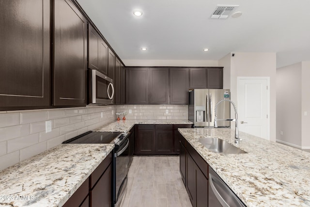 kitchen featuring appliances with stainless steel finishes, light stone countertops, dark brown cabinetry, and sink