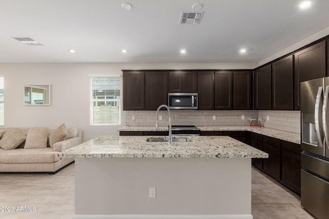 kitchen with sink, dark brown cabinets, a kitchen island with sink, stainless steel appliances, and decorative backsplash