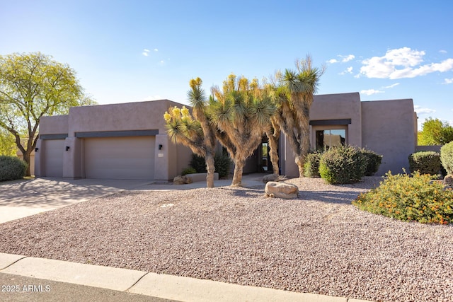 pueblo-style home featuring an attached garage, concrete driveway, and stucco siding