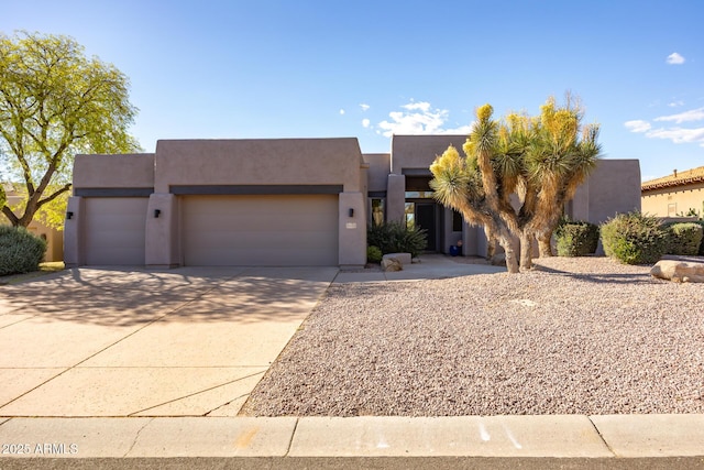 pueblo revival-style home with a garage, concrete driveway, and stucco siding