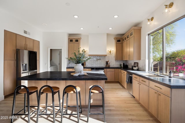 kitchen featuring a kitchen breakfast bar, stainless steel appliances, a sink, light wood finished floors, and a center island