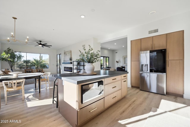 kitchen with stainless steel refrigerator with ice dispenser, light wood finished floors, dark countertops, a kitchen island, and recessed lighting