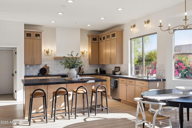 kitchen featuring dark countertops, dishwasher, a kitchen island, a kitchen breakfast bar, and light wood-type flooring