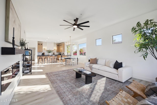 living area with a ceiling fan, light wood-style floors, a chandelier, and baseboards