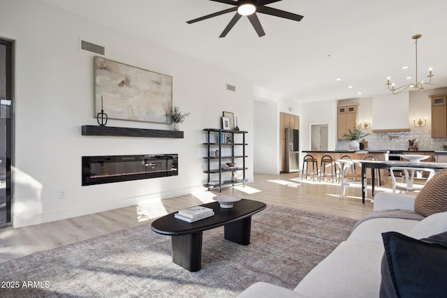 living area with light wood-type flooring, a ceiling fan, a glass covered fireplace, a chandelier, and recessed lighting