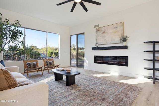 living room with a glass covered fireplace, wood finished floors, and ceiling fan