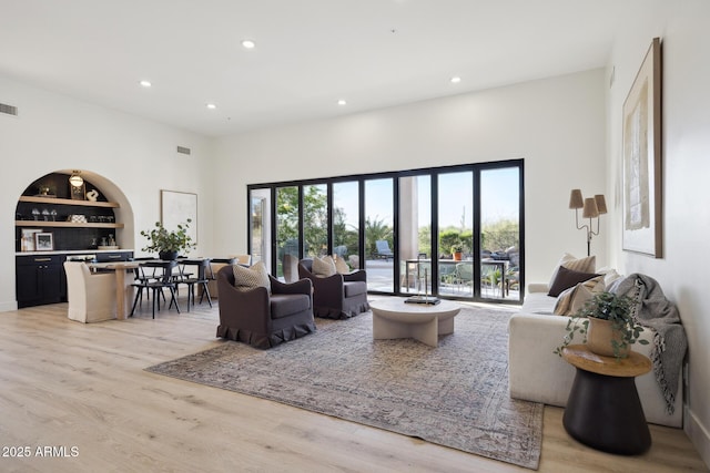 living area featuring recessed lighting, light wood-style flooring, built in shelves, and a towering ceiling