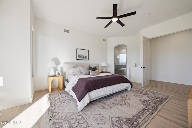 bedroom with arched walkways, wood finished floors, baseboards, a ceiling fan, and ensuite bathroom