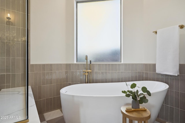 bathroom with tile walls, a soaking tub, and a wainscoted wall