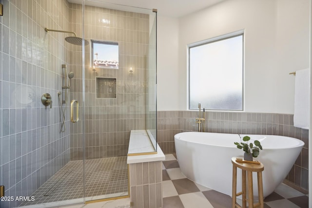 full bath featuring tile walls, a shower stall, a freestanding tub, wainscoting, and tile patterned floors