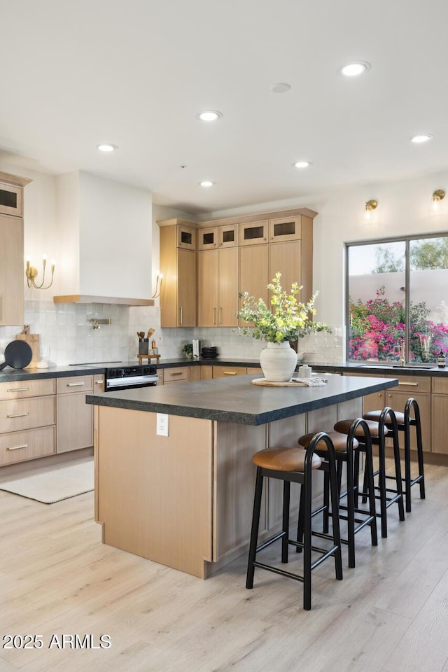 kitchen with light brown cabinetry, dark countertops, light wood finished floors, a kitchen island, and recessed lighting