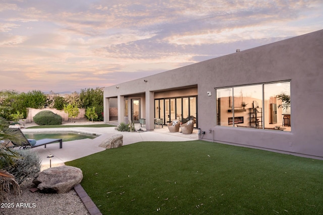 back of house at dusk featuring a patio area, stucco siding, and an outdoor pool